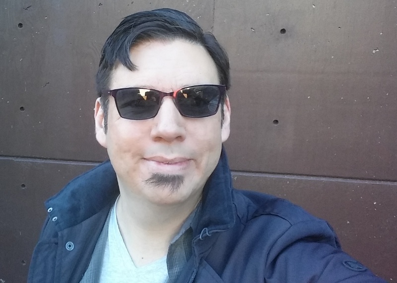 Selfie in sunglasses against a dark panel wall.