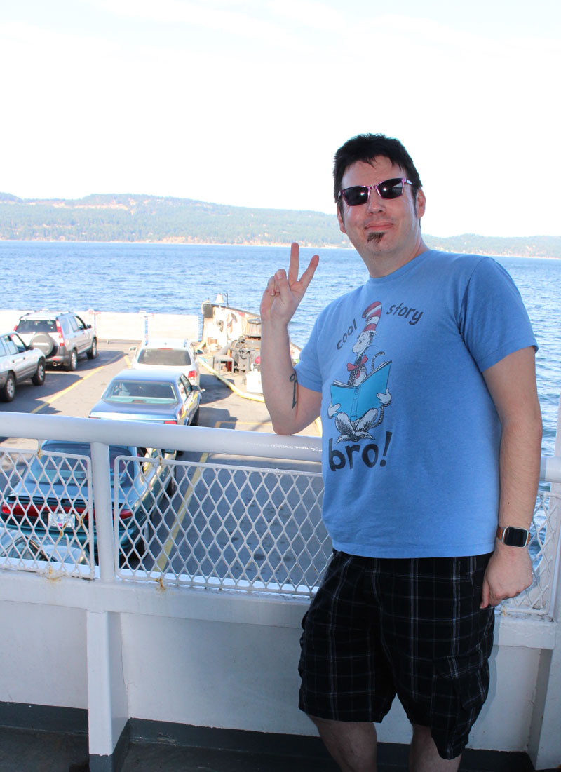 Glenn flashing a peace sign on the deck of a car ferry, water behind.
