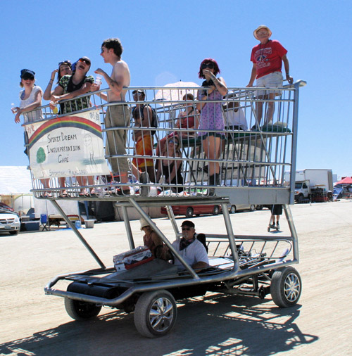 A crowd riding a shopping-cart go-kart at a desert gathering.